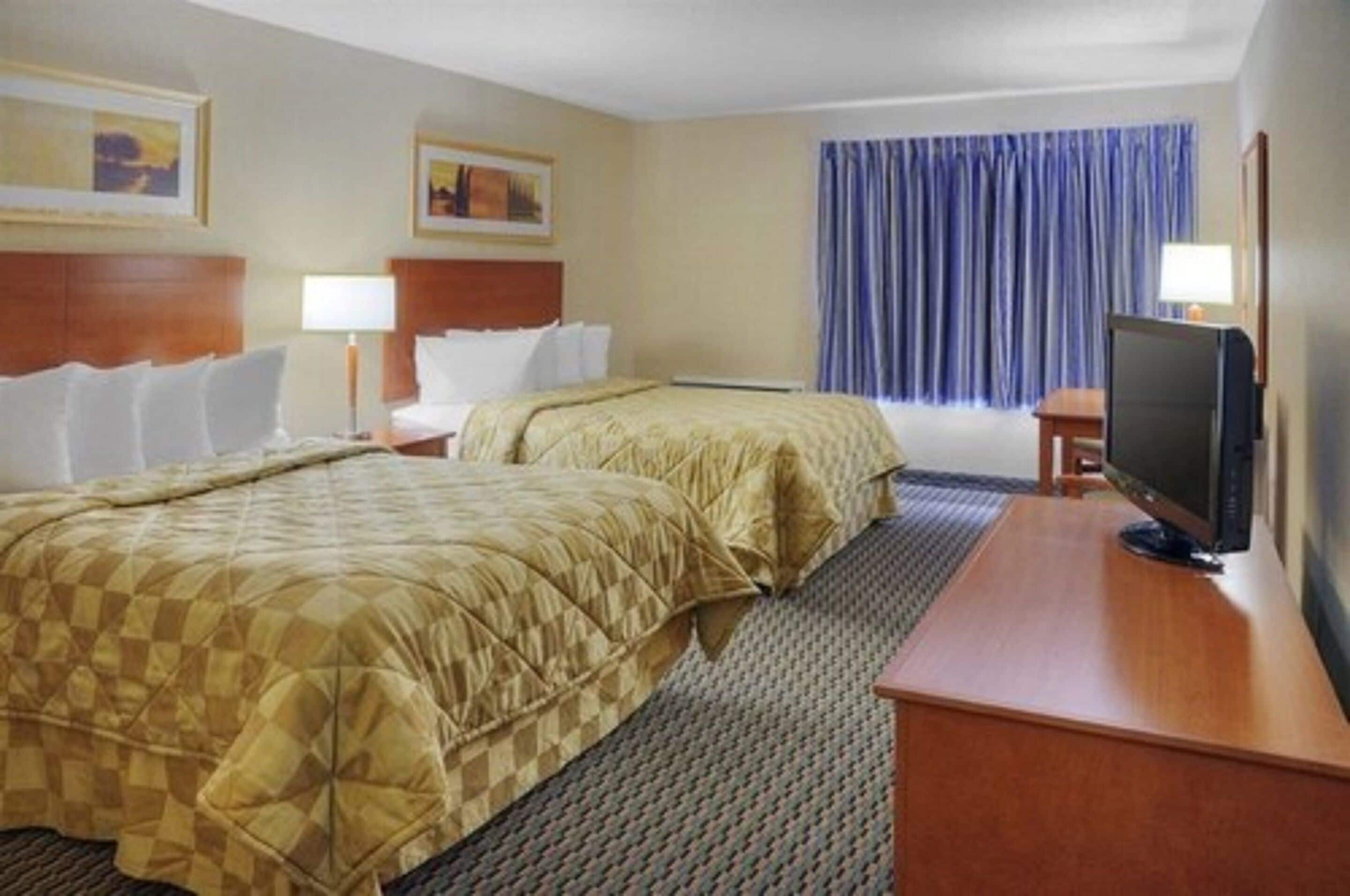 Une chambre d’hôtel avec deux lits, une télévision et une fenêtre avec des rideaux.