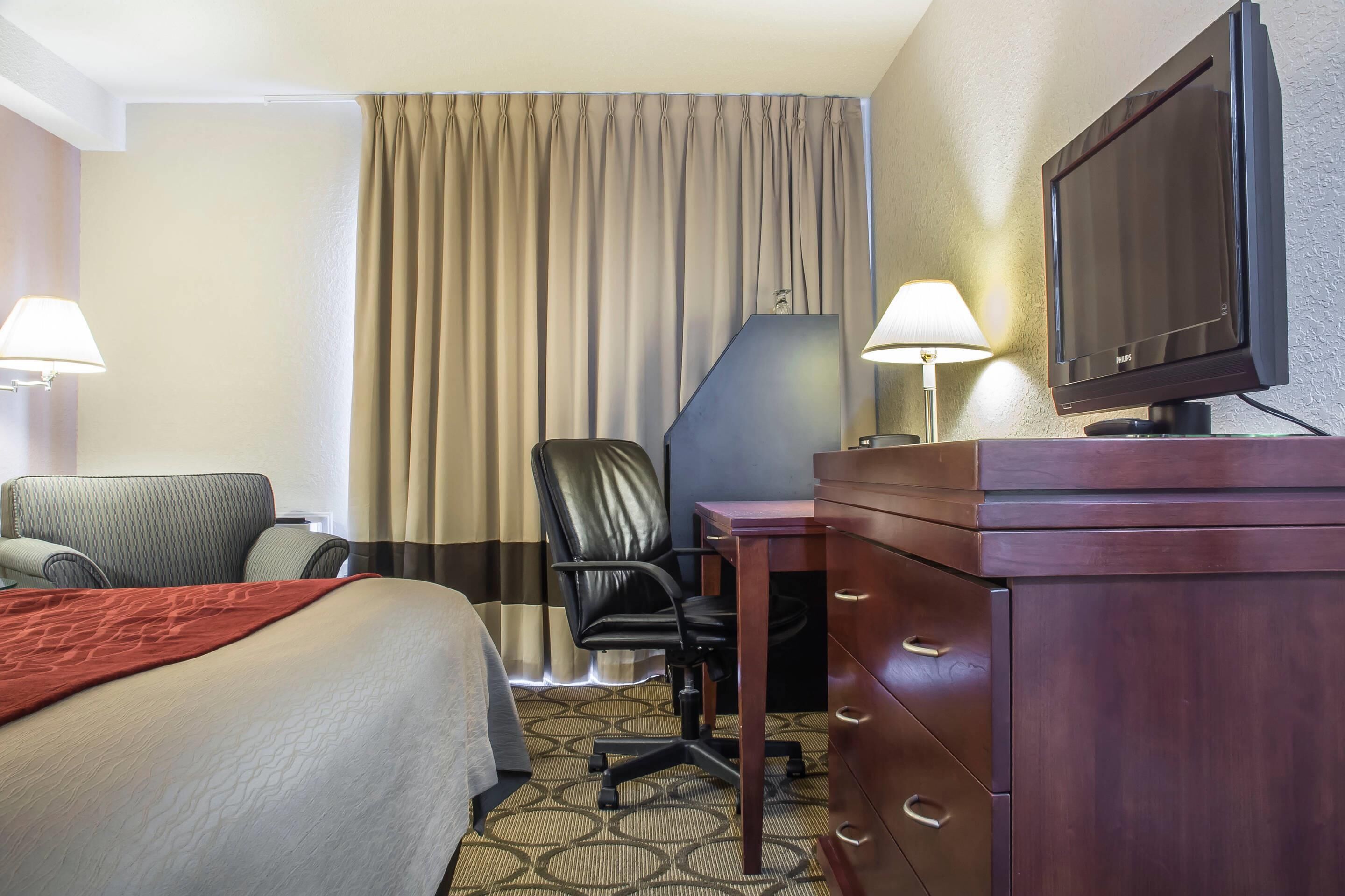 Ein Hotelzimmer mit einem Bett, einem Schreibtisch mit Fernseher, einem Sessel und einer Lampe.