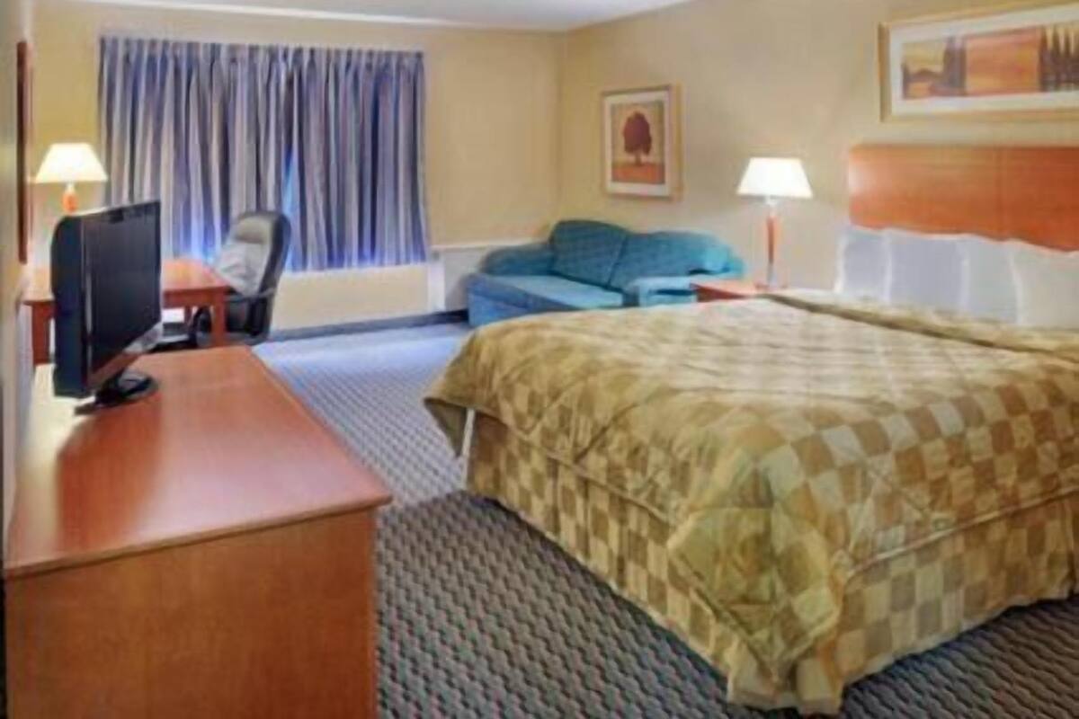 A hotel room with a bed, a desk, a chair, a television, and a window with curtains.