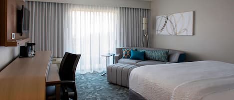 A hotel room with a large bed, a sofa, a desk, and a TV.