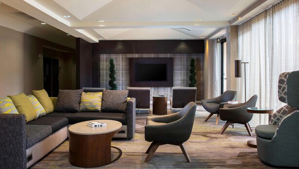A modern hotel lobby with a sectional sofa, armchairs, a round coffee table, and a flat-screen TV mounted on the wall. - Sonesta Select Atlanta Norcross (Norcross)