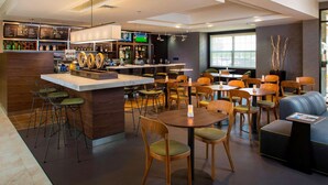 A modern bar area with a counter, stools, and a seating area with round tables and chairs. - Sonesta Select Atlanta Norcross (Norcross)