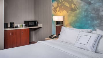 A hotel room with a bed, a nightstand with a lamp, a microwave, and a coffee maker on the counter.