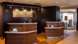 A reception area with two wooden reception desks, a large abstract painting on the wall, and a seating area with a lamp and chairs. - Sonesta Select Atlanta Norcross (Norcross)