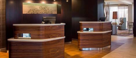 A reception area with two wooden reception desks, a large abstract painting on the wall, and a seating area with a lamp and chairs.