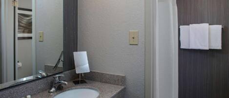 A bathroom with a granite countertop, a sink, a mirror, and a towel rack.