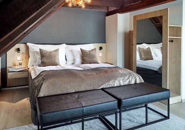 A modern bedroom with a large bed, a bench, and a wooden ceiling.