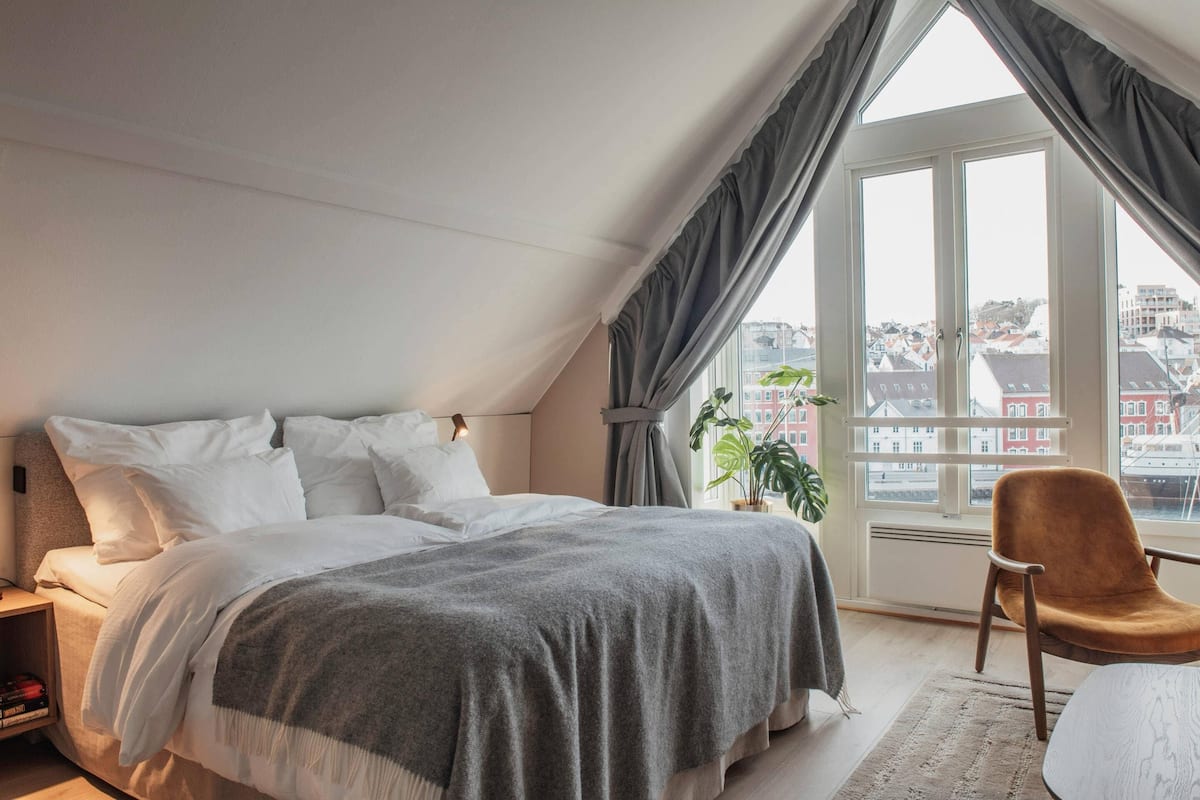A bedroom with a large window, a bed, a chair, and a nightstand.