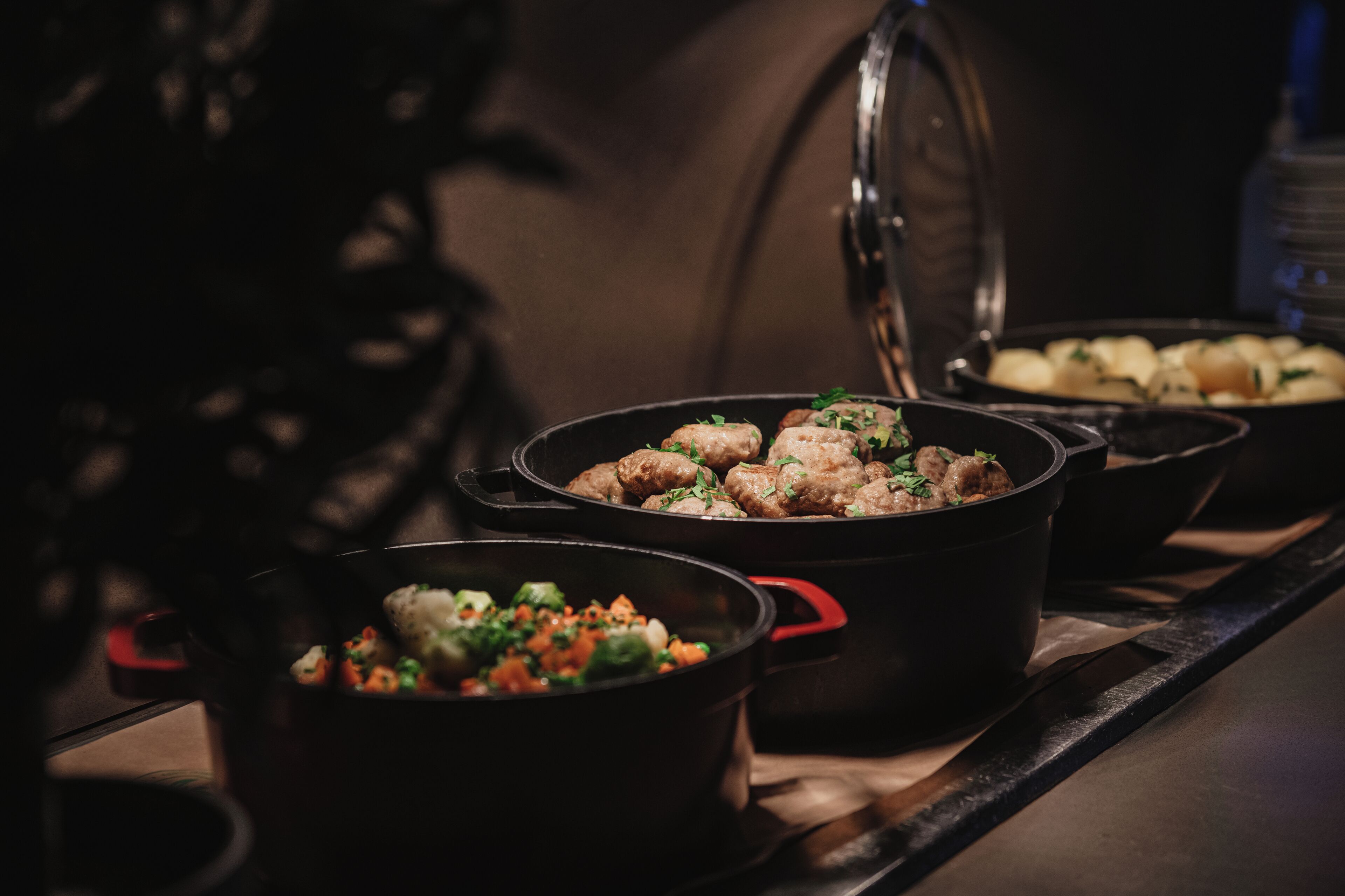 A kitchen with multiple pots on a stove, one containing meatballs and another with a vegetable mix.