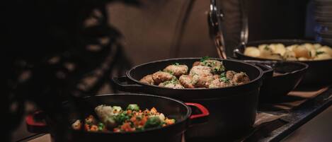 A kitchen with multiple pots on a stove, one containing meatballs and another with a vegetable mix.