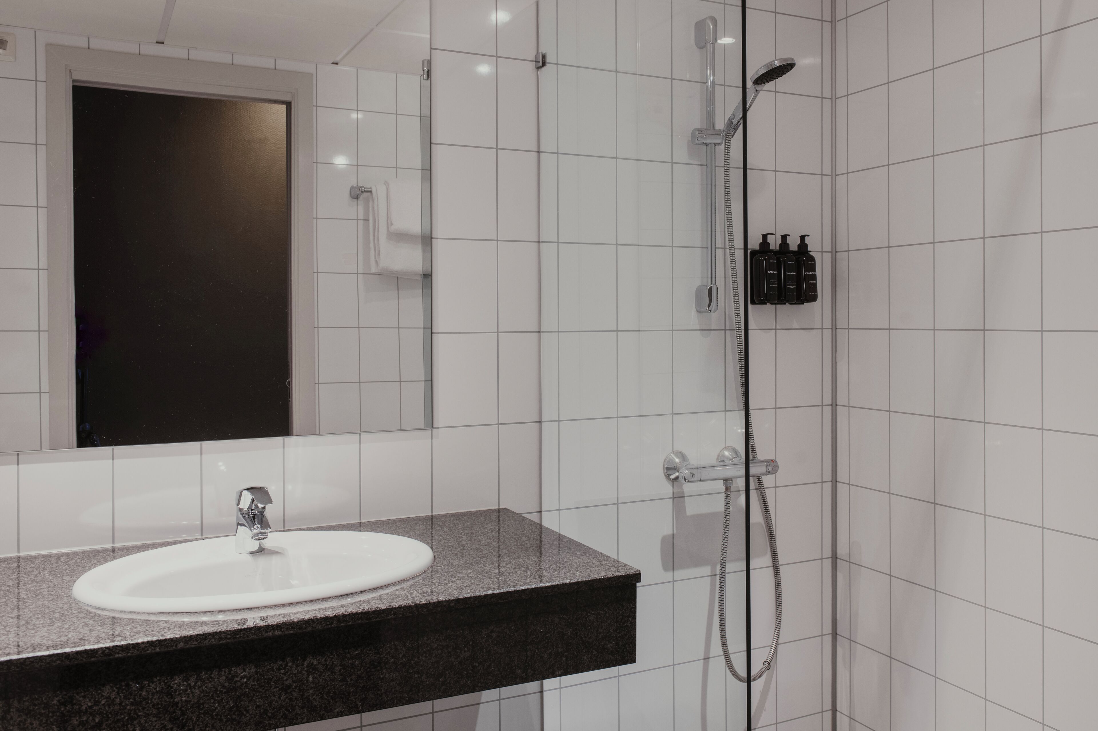 A bathroom with a white sink, a mirror, a shower, and a towel rack.