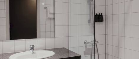 A bathroom with a white sink, a mirror, a shower, and a towel rack.