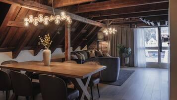 A dining area with a wooden table and chairs, a sofa, and a hanging light fixture.