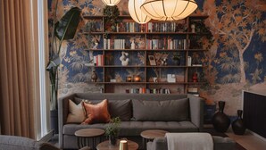 A cozy living room with a grey sofa, a bookshelf filled with books, and a large wall mural. - Home Hotel Skagen Brygge (Stavanger)