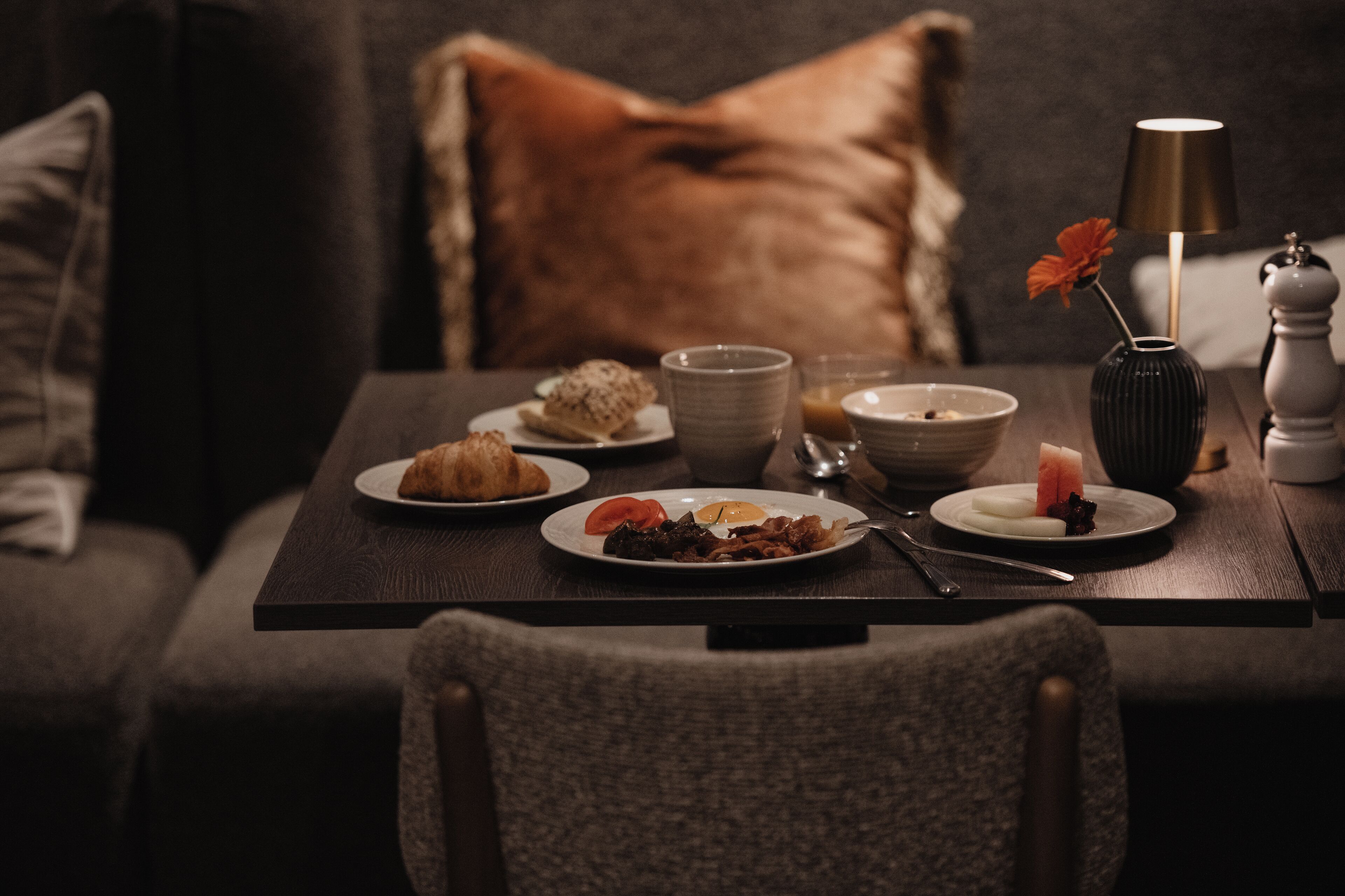 A dining table with plates of food, a vase with a flower, and a lamp.