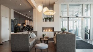 A modern hotel lobby with sofas, a fireplace, pendant lights, and a view through large glass doors. - Home Hotel Skagen Brygge (Stavanger)