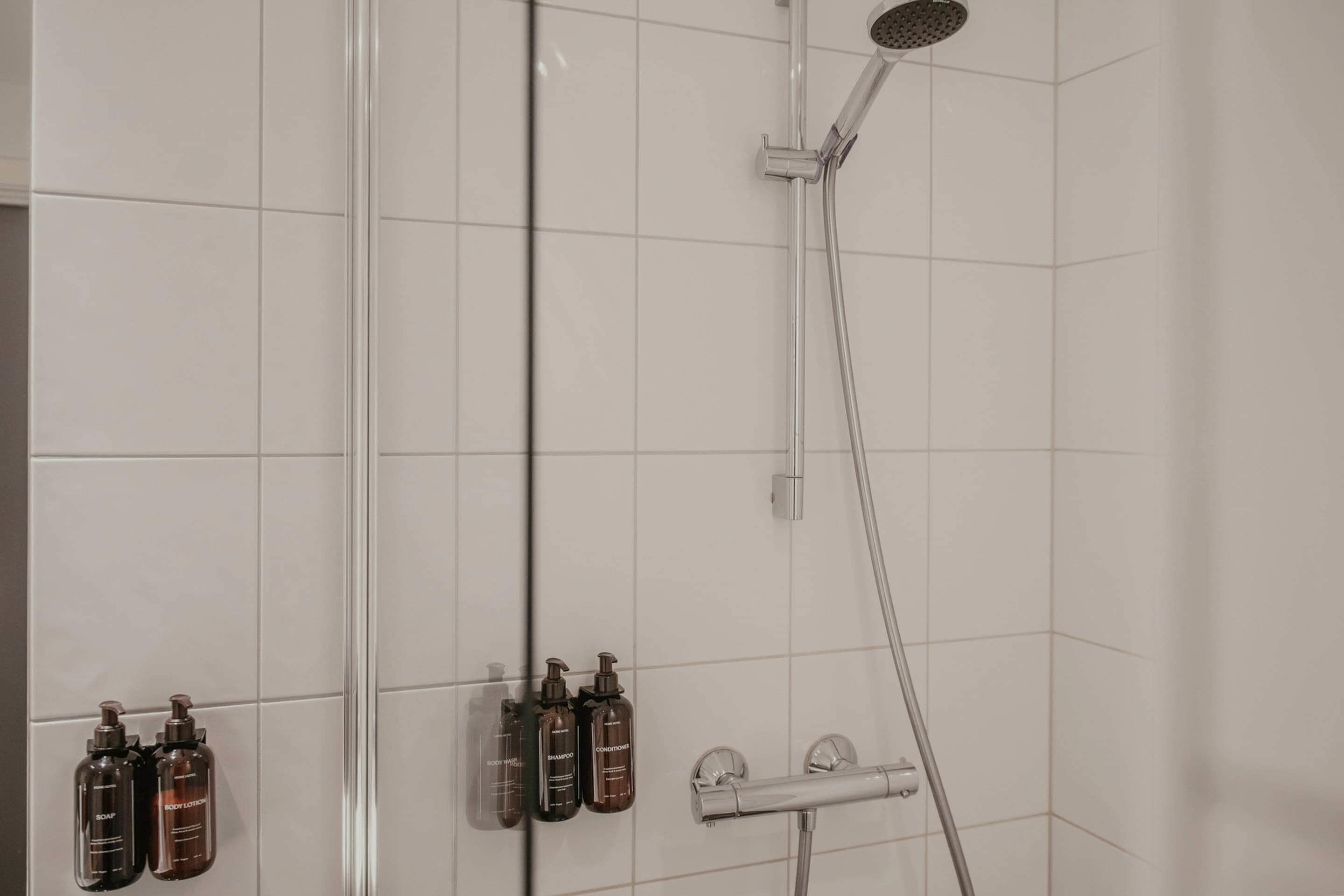 Une douche équipée d’un pommeau de douche à main, d’un robinet mural et de trois bouteilles de shampoing et d’après-shampoing.