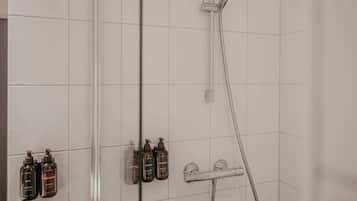 Een douche met een handdouche, een wandmengkraan en drie flessen shampoo en conditioner.