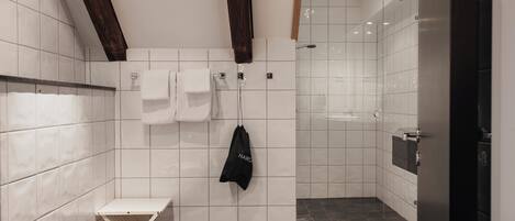 A modern bathroom with white tiles, a shower, a bench, and a towel rack.