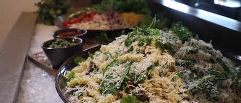 Un bufé con diversos platos, como pasta con queso y vegetales verdes, y otras ensaladas.