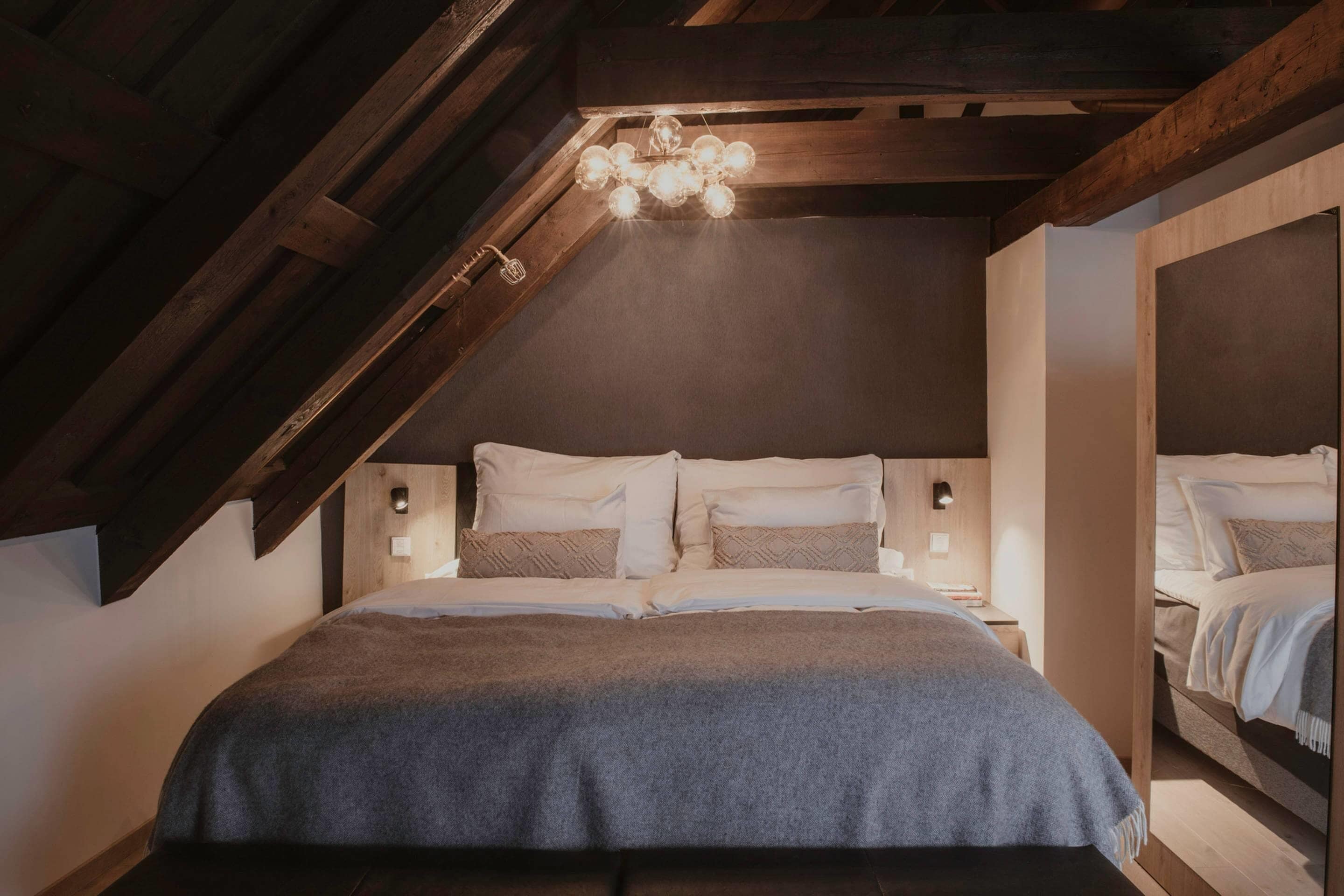 Un dormitorio con techo inclinado, una araña, una cama con almohadas y una mesita de noche.