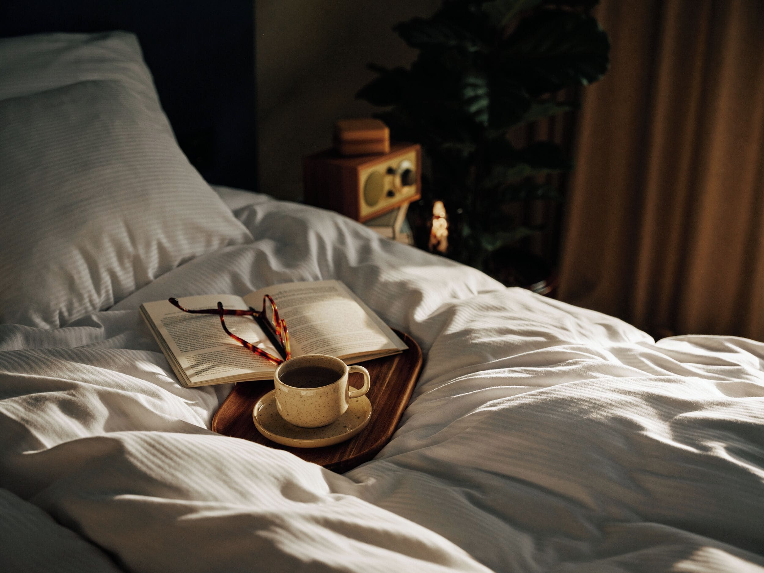 Una cama con un libro, gafas y una taza sobre una bandeja.