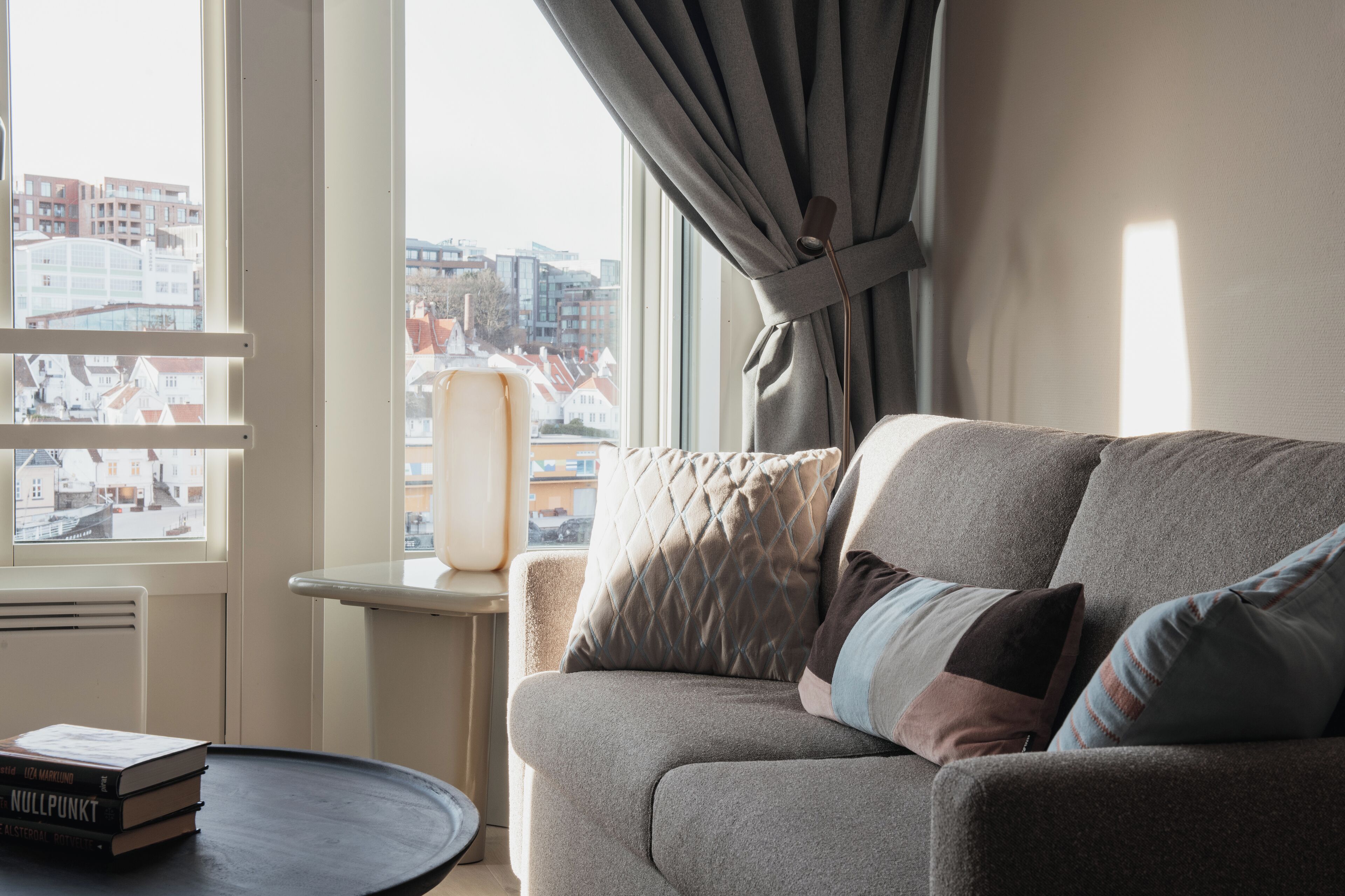 Un salon avec un canapé, une petite table, une fenêtre avec des rideaux et une vue sur les bâtiments à l’extérieur.