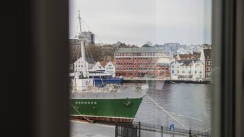 A harbor with a green ship named 'SANDNES' docked, buildings in the background, and a view through a window.