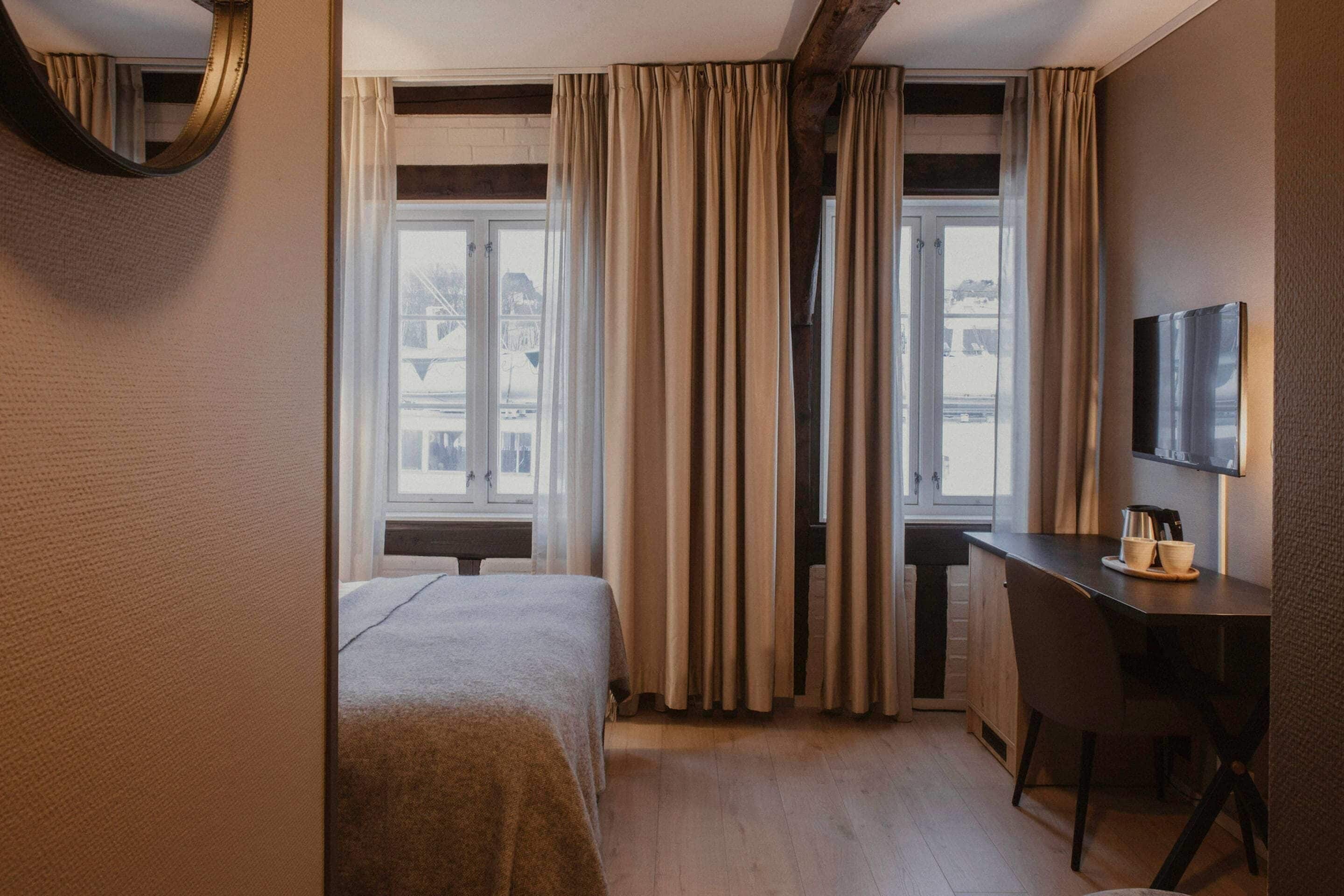 Een hotelkamer met een bed, een bureau, een stoel, een televisie en een raam met gordijnen.