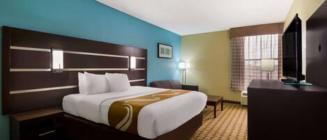 Quarto de hotel com uma cama grande, uma escrivaninha, televisão e janela com cortinas.