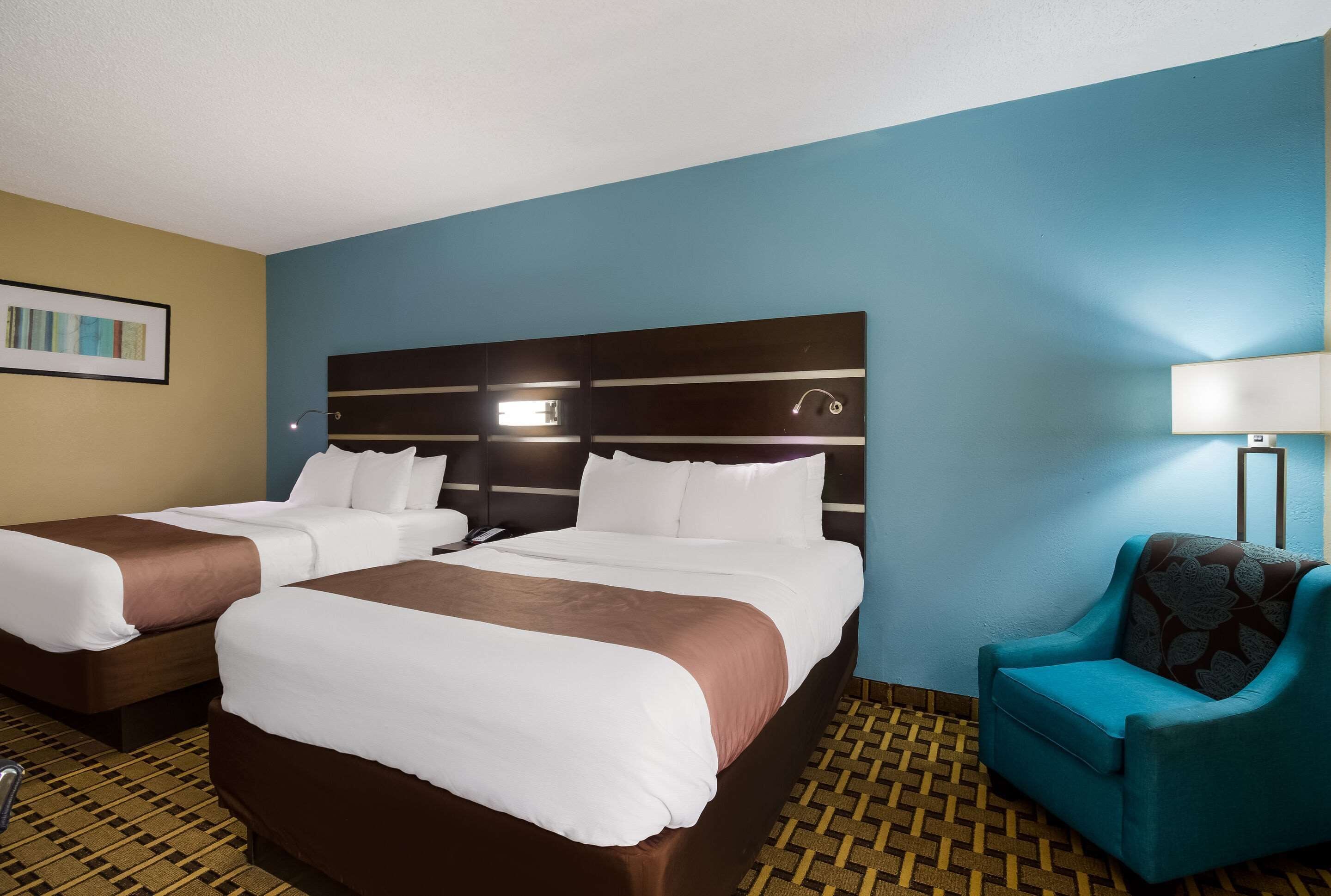 A hotel room with two beds, a blue armchair, and a patterned floor.