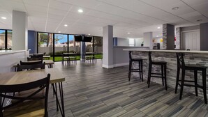 A modern indoor dining area with wooden tables and chairs, a stone accent wall, and a large window providing a view of the outdoors.
