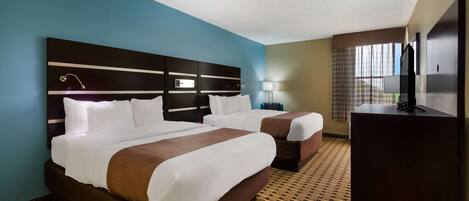 A hotel room with two beds, a desk, a TV, and a window with curtains.