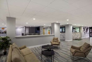 A modern lobby with a reception desk, seating area, and a kitchen in the background. - Quality Inn Houston East I-10 (Houston)