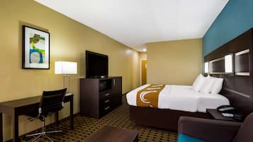 A hotel room with a bed, desk, chair, TV, and a painting on the wall.