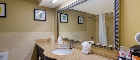 A bathroom with a sink, mirror, towel dispenser, and toiletries.