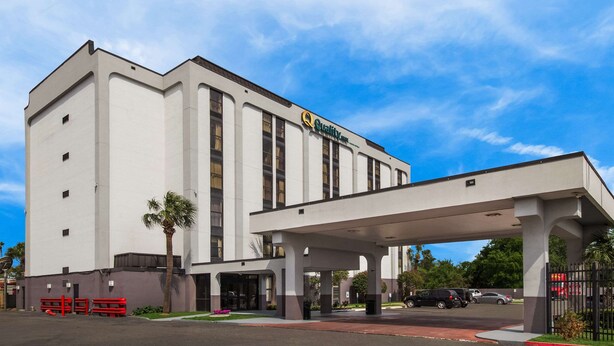 A hotel with a white facade, a covered entrance, and a parking lot with several cars.