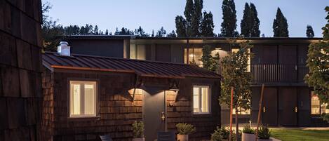 A wooden cabin with a fire pit and outdoor seating, surrounded by a landscaped garden and tall trees.