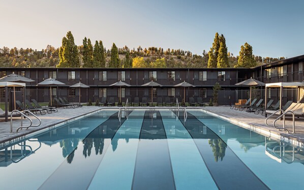 A modern hotel with a large pool, outdoor seating, and a view of trees. - High Country Motor Lodge – Near NAU/Downtown (Flagstaff)