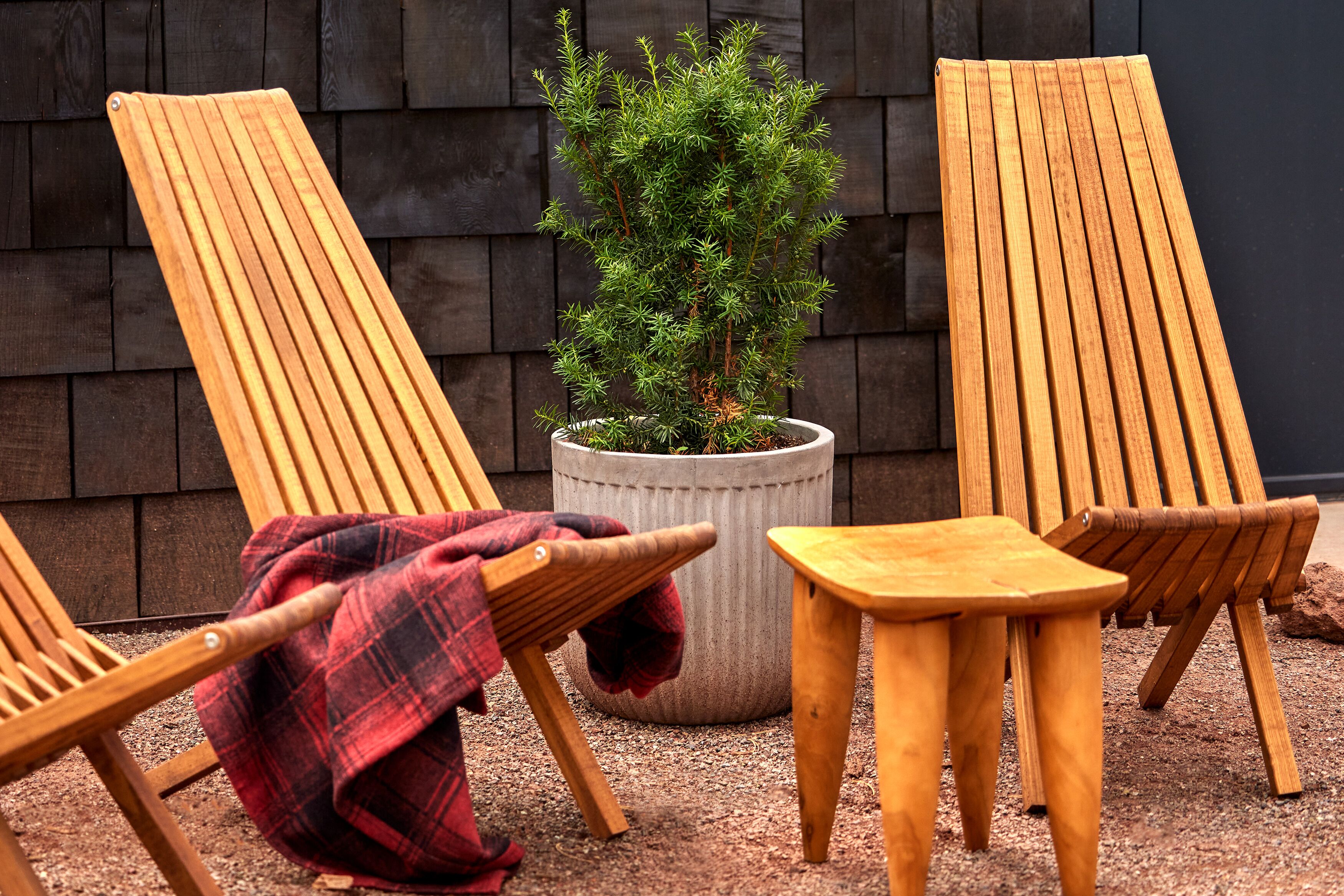 Zwei Holzliegen und ein kleiner Holztisch draußen, mit einem Blumentopf.