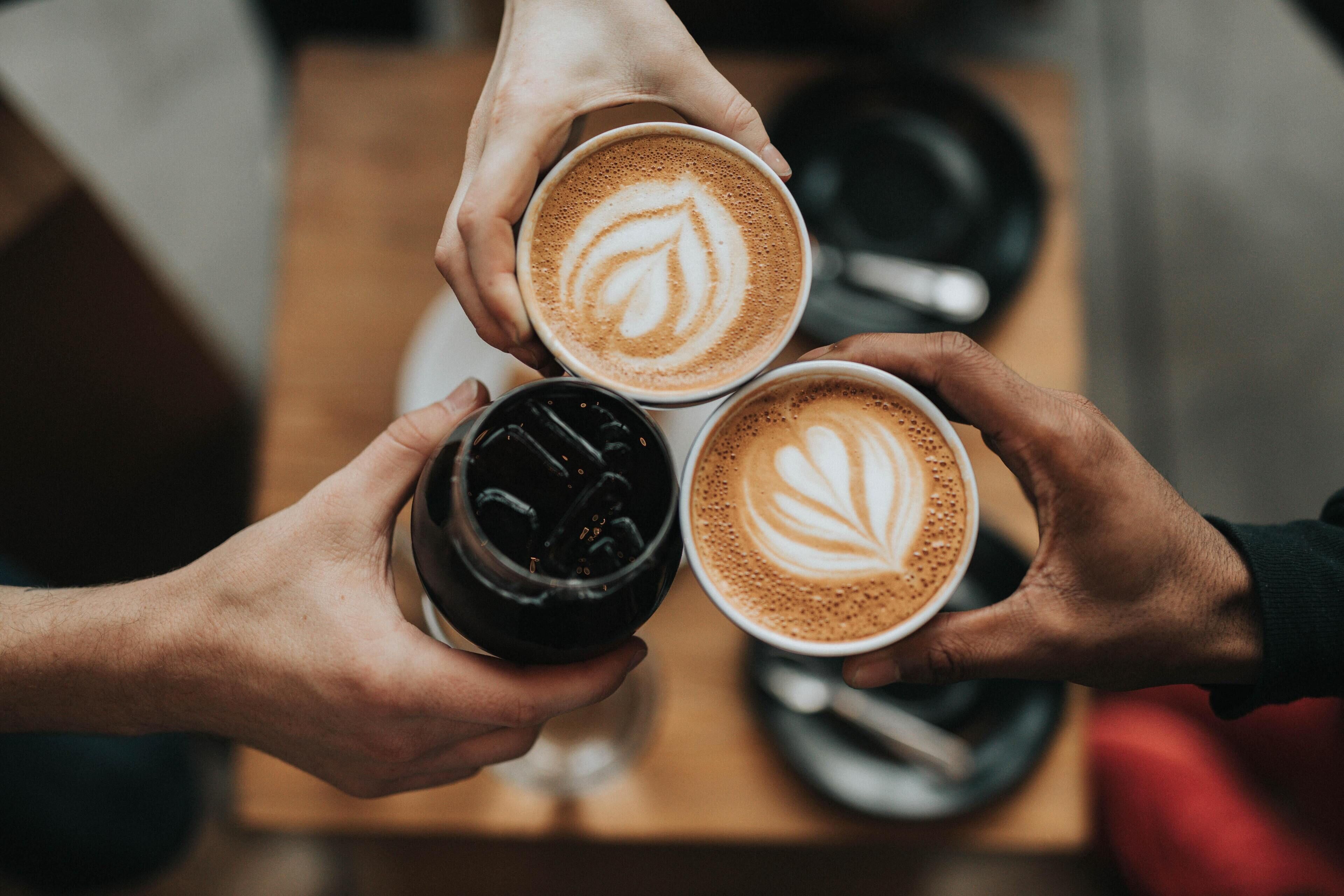 Trois tasses de café décorées de motifs en latte art, tenues dans des mains.