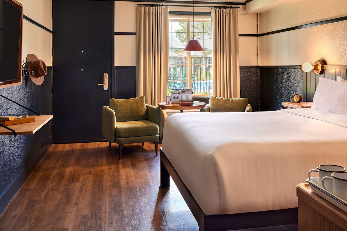 A hotel room with a large bed, two armchairs, a desk with a lamp, a radio, and a view of the outdoors through the window.