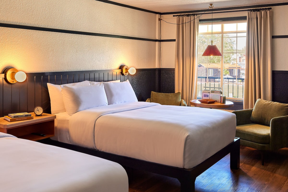 A hotel room with a large bed, two bedside tables with lamps, a chair, and a view of the outside.