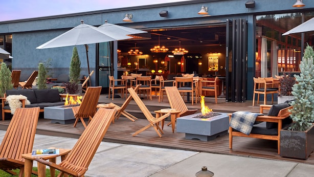An outdoor seating area with wooden chairs and tables, a fire pit, and umbrellas. - High Country Motor Lodge – Near NAU/Downtown (Flagstaff)