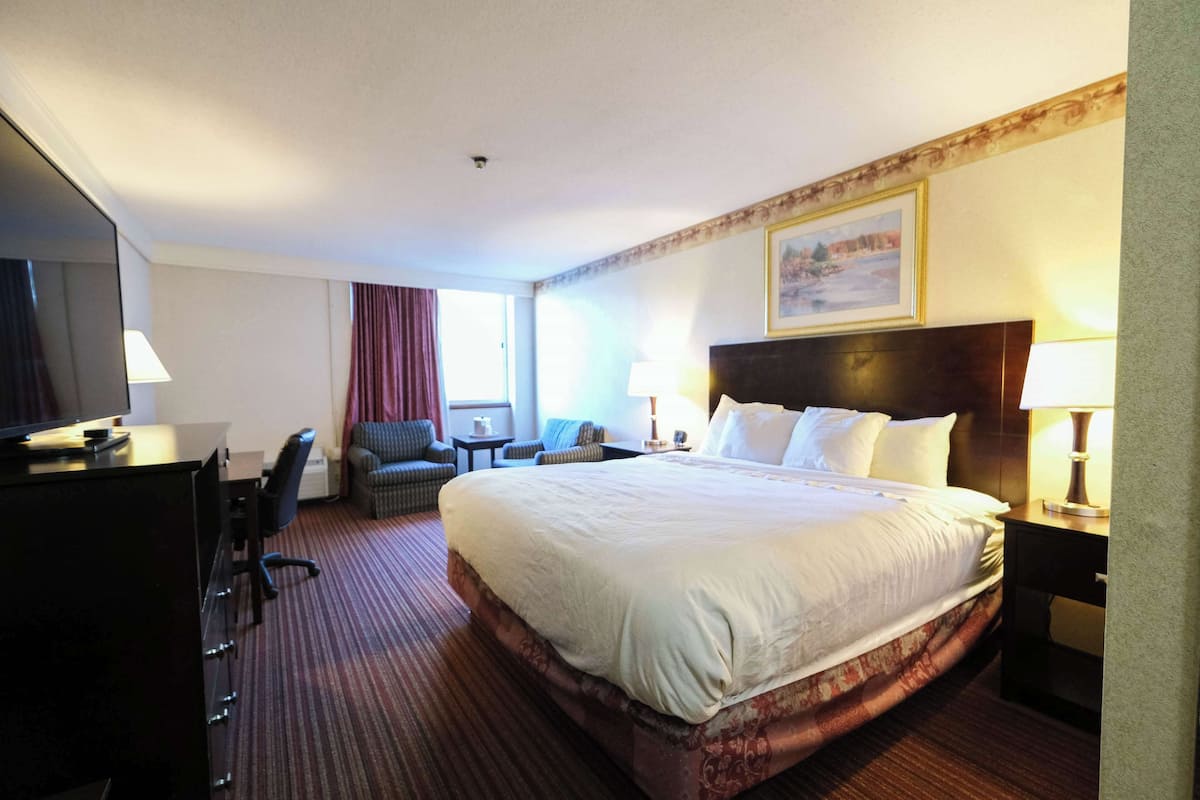 Quarto de hotel com cama grande, escrivaninha, cadeira, mesa pequena e televisão.