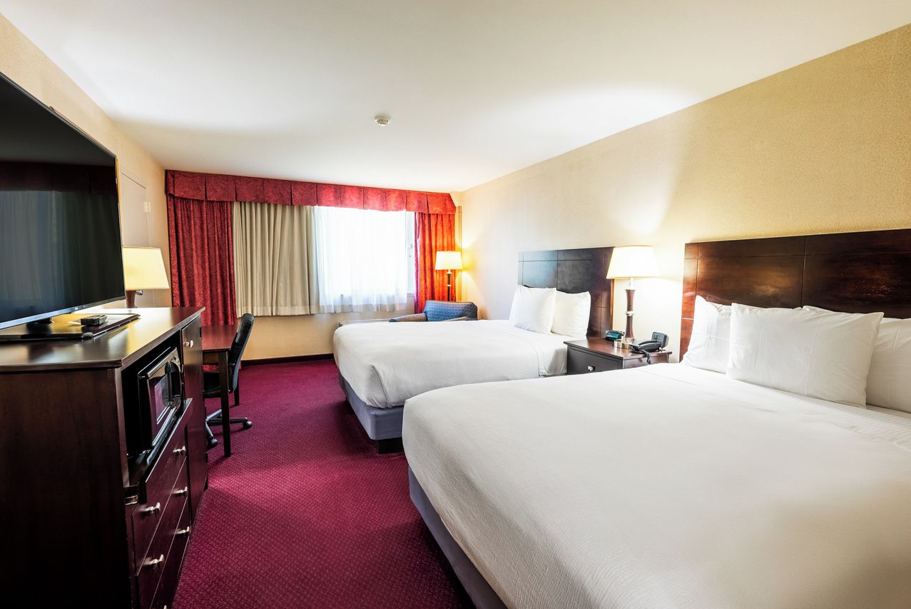 Een hotelkamer met twee bedden, een bureau, een televisie en een raam met gordijnen.