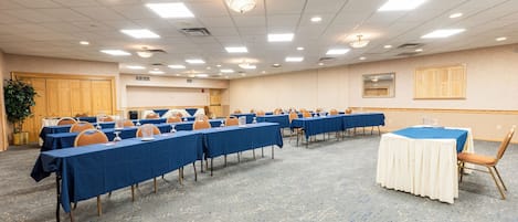 Un salón de conferencias con filas de mesas y sillas, piso alfombrado e iluminación empotrada en el techo.