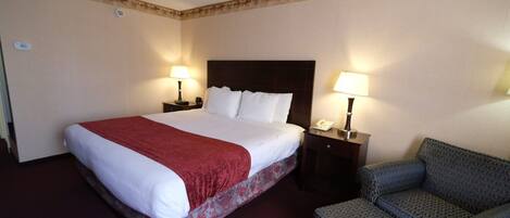 A hotel room with a large bed, two bedside tables with lamps, and a patterned armchair.