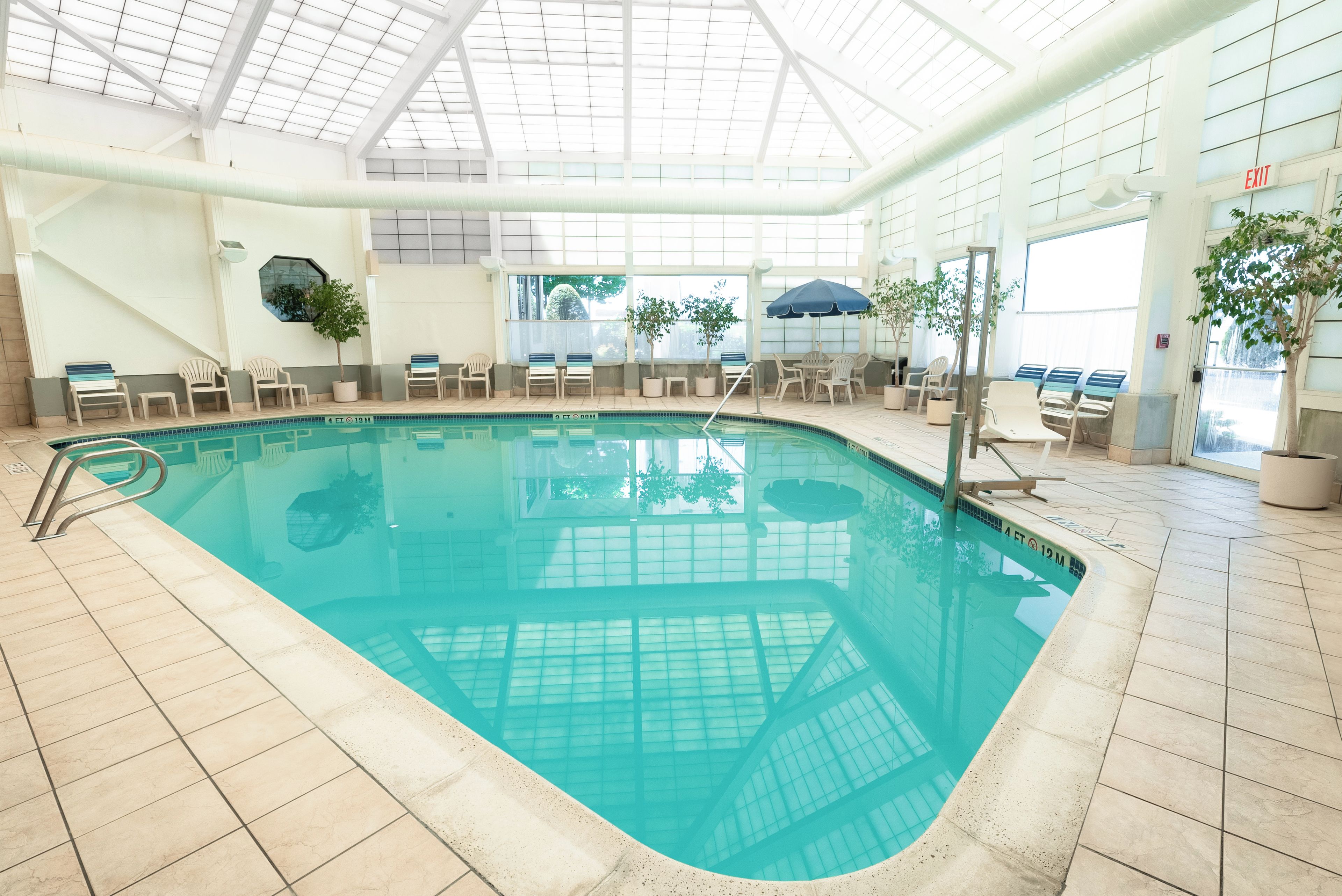 An indoor swimming pool with clear water, surrounded by lounge chairs and potted plants.
