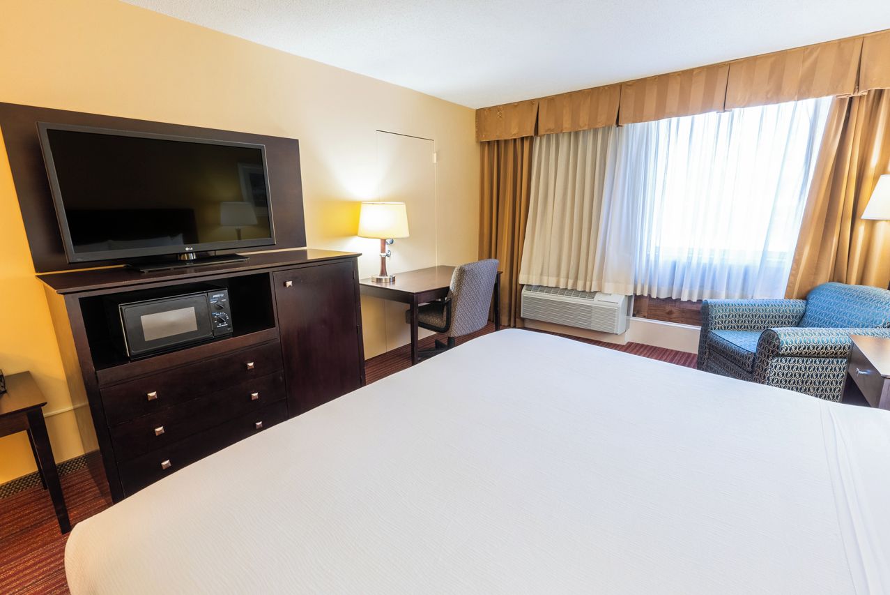 Une chambre d’hôtel avec un grand lit, un téléviseur à écran plat, un bureau avec une lampe, une chaise et une fenêtre avec des rideaux.